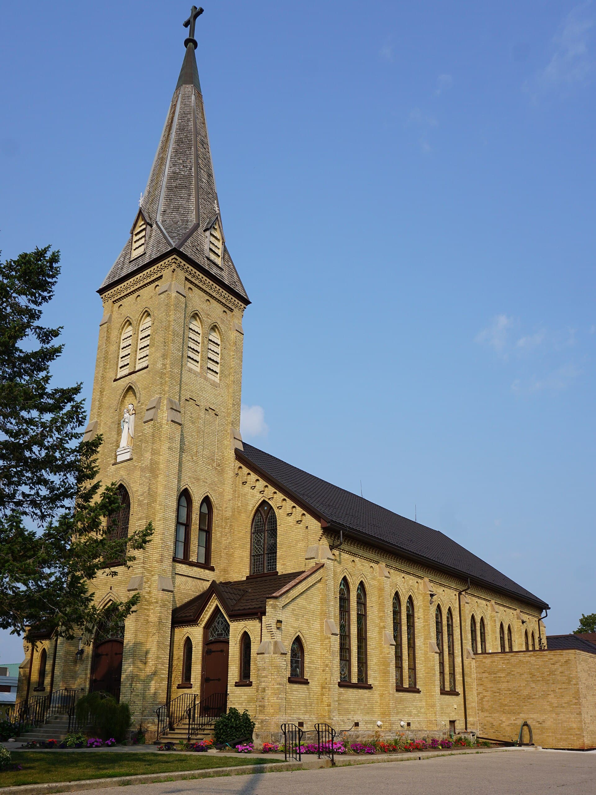 Holy Family Church's buff-brick spire in New Hamburg, evening light on the flower beds